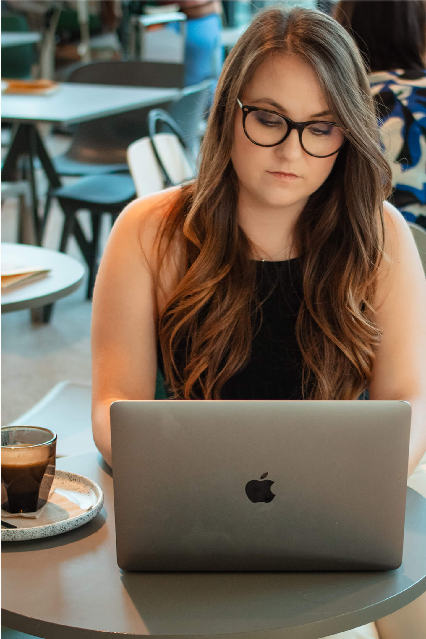 Nő fekete ruhában laptop előtt ül, cappuccinóval