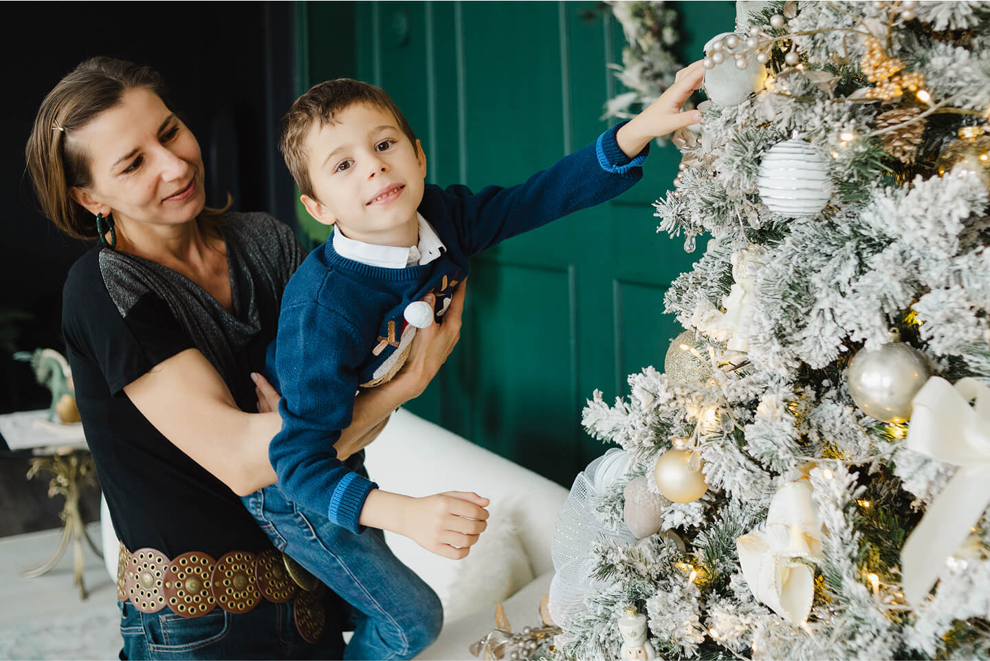 Mother and son decorating a Christmas tree with snow-covered ornaments.