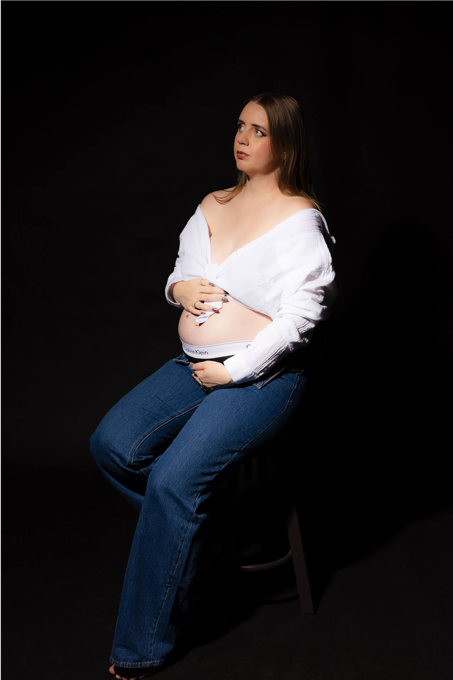 Kismama ülve, farmerban és ingben, tekintete felfelé irányul.
