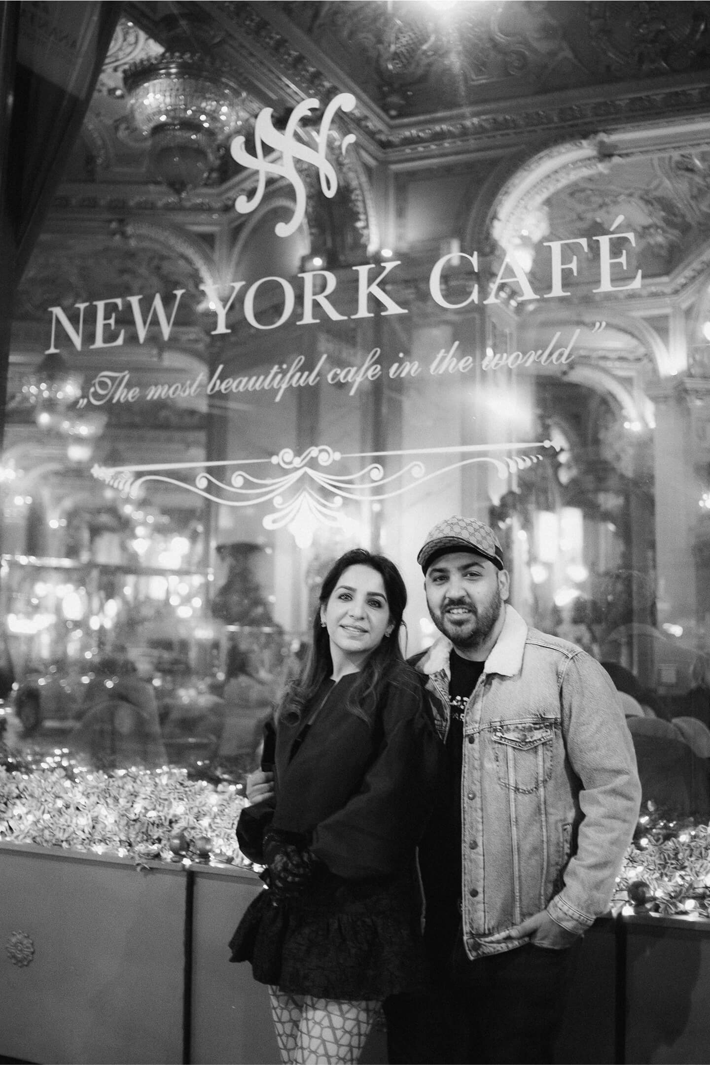 Pár pózol a New York Café kirakatában, ünnepi fények között