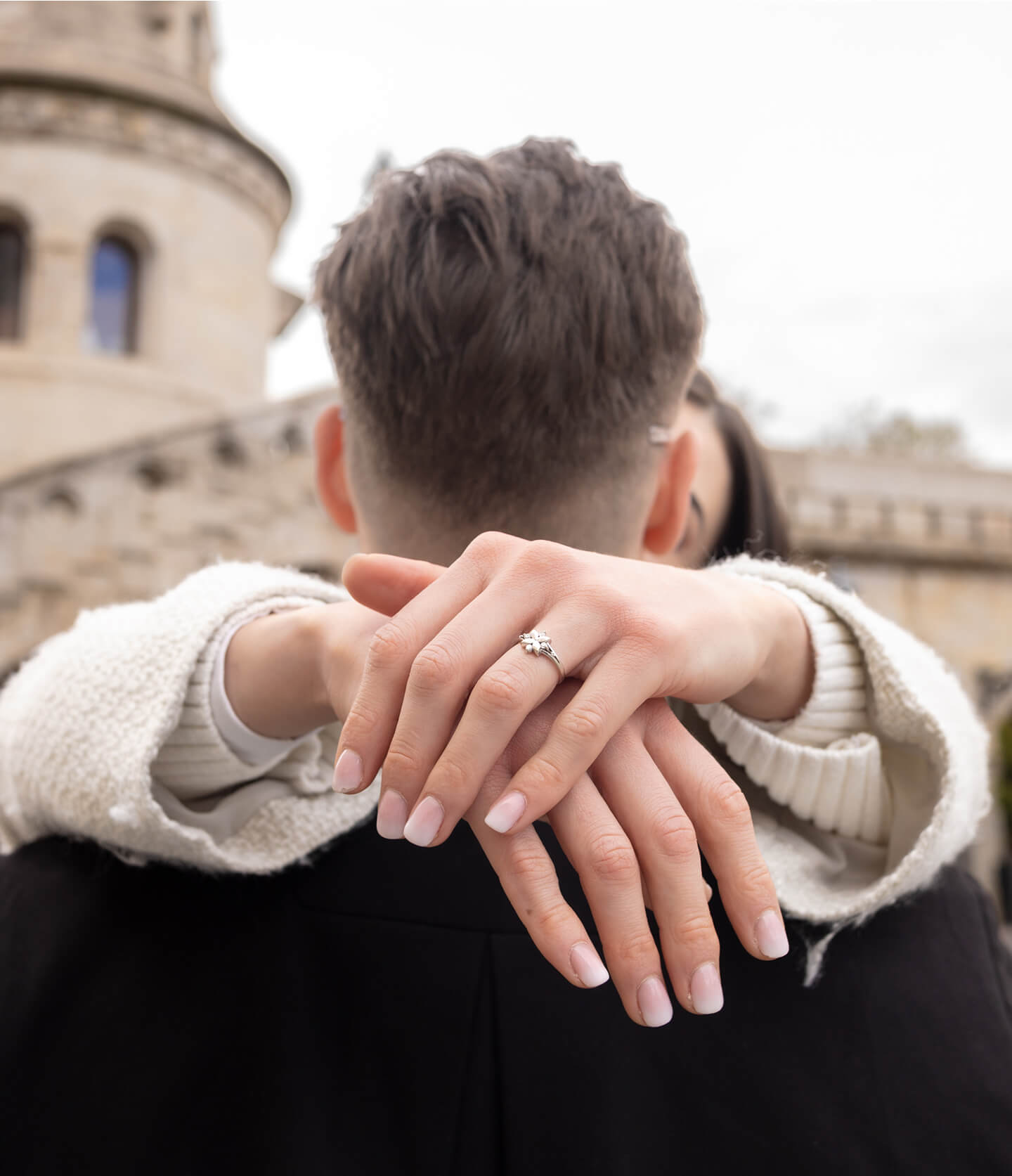 The bride's hands with a ring resting on the groom's shoulder.