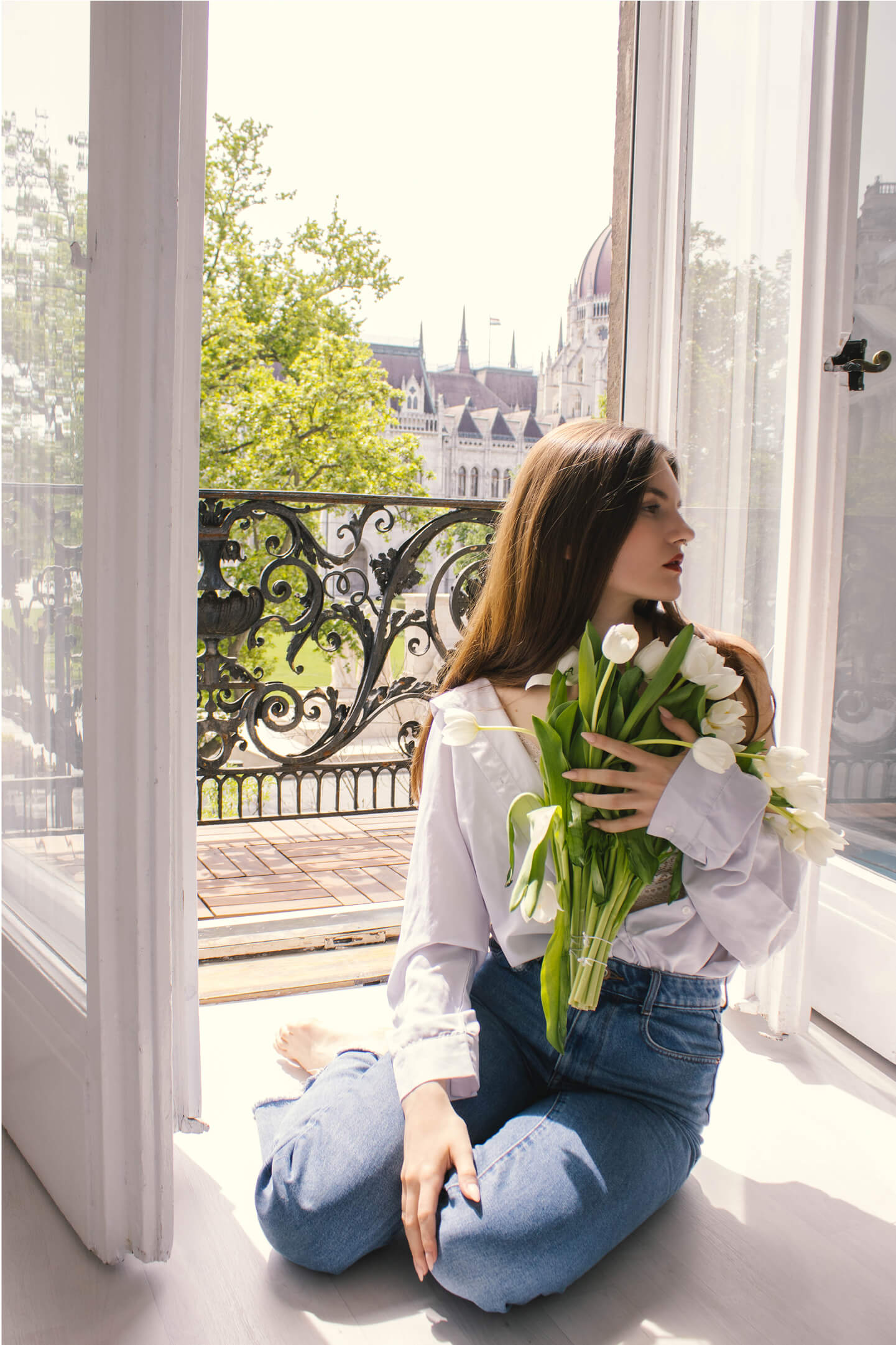 Woman sitting on the floor with a bouquet of white tulips, with the Budapest Parliament in the background.