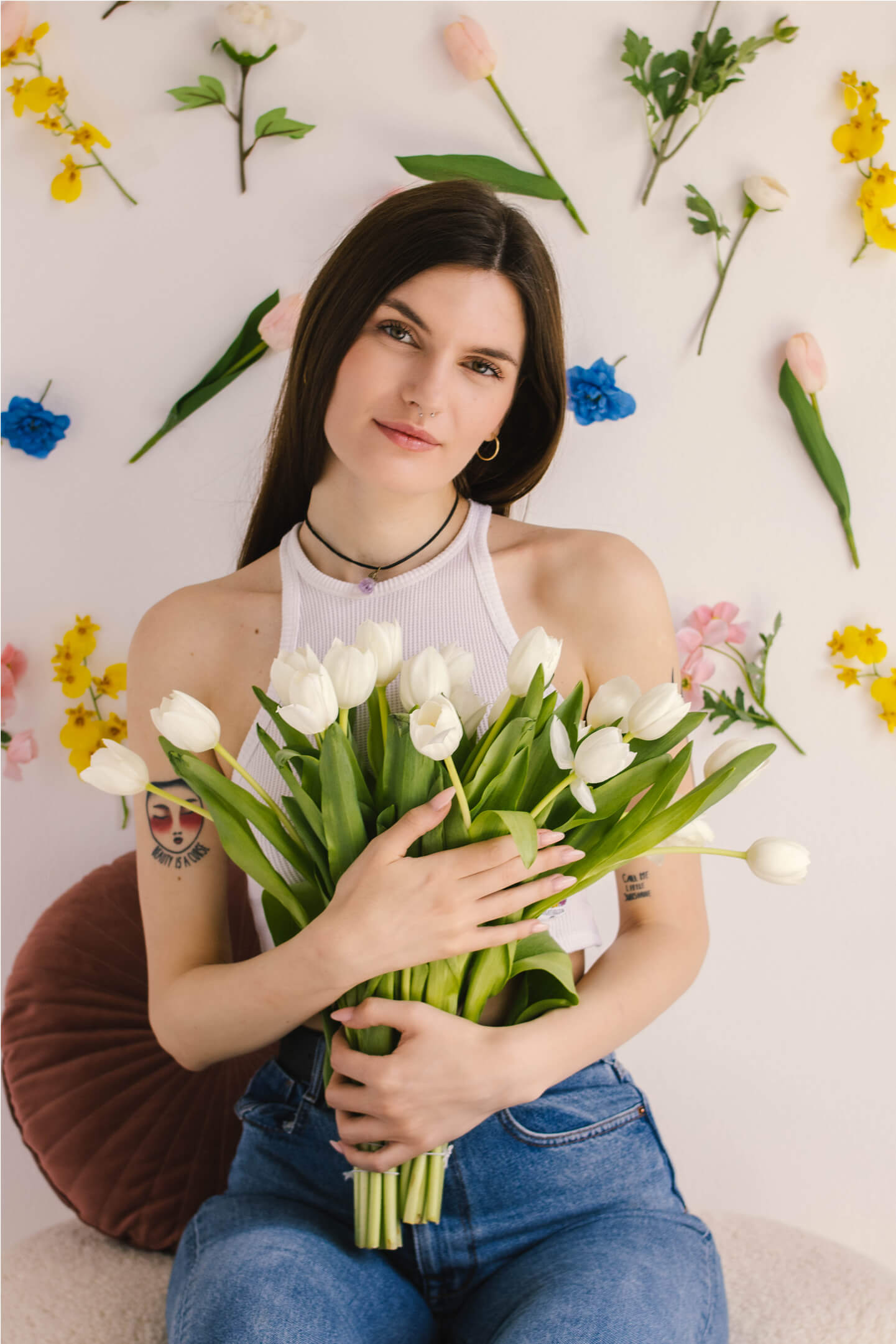 Mosolygó nő fehér tulipáncsokorral, színes virágos háttér előtt